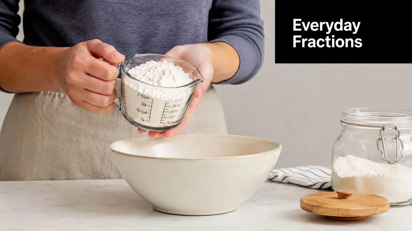 A person holding a glass measuring cup filled with white flour over a large ceramic bowl.