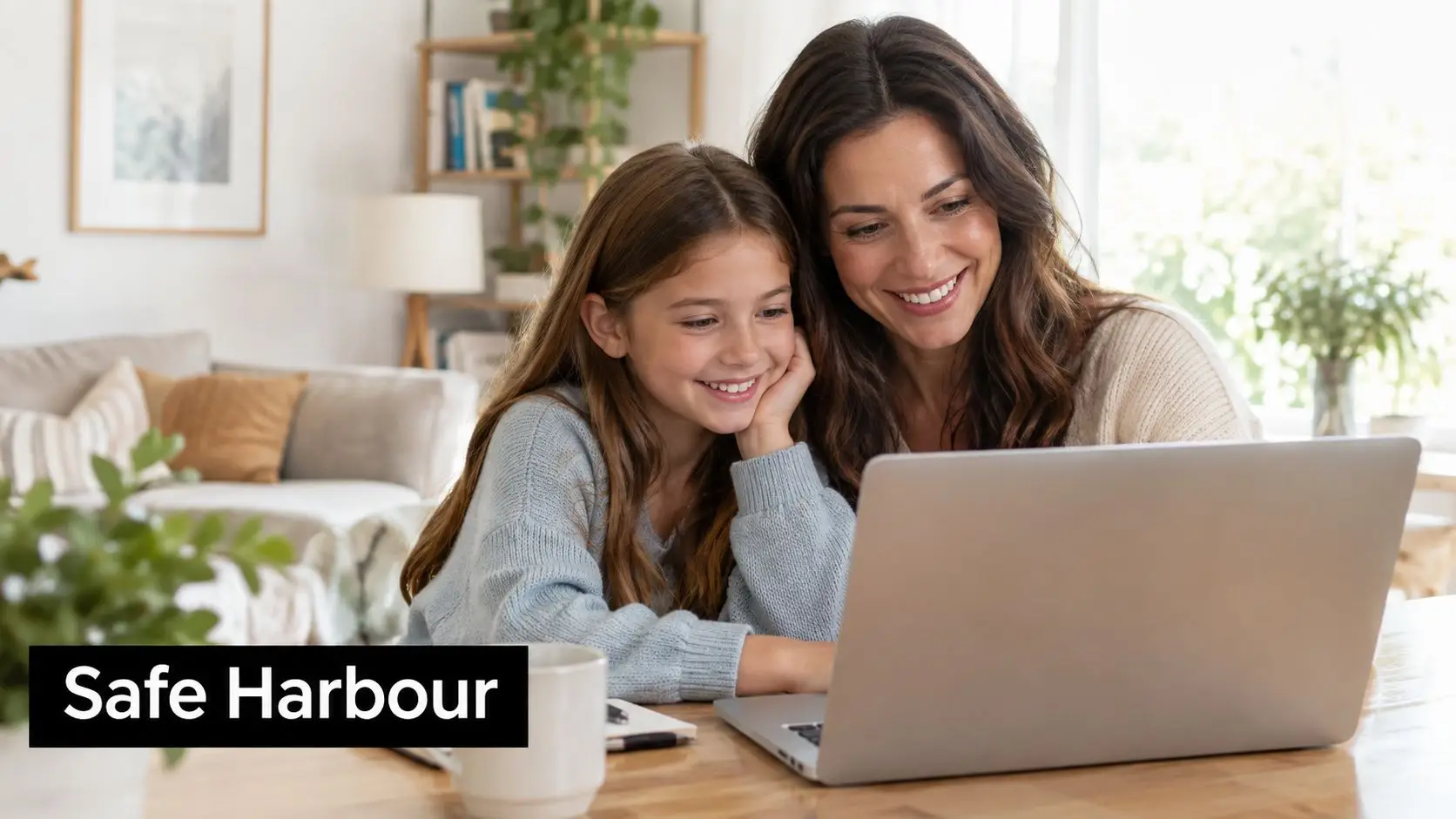 A mother and her young daughter sitting at a table together while looking at a laptop computer.